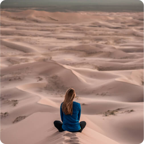 Person standing alone in a vast, beautiful desert with golden sand dunes under a clear blue sky.
